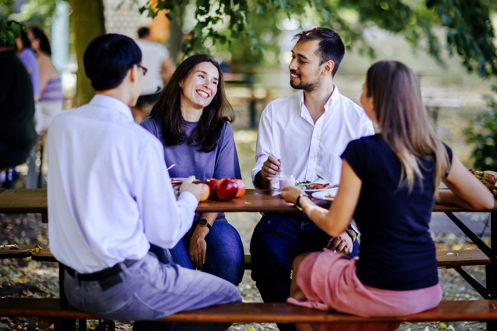 Kolleg*innen, die gemeinsam drau&szlig;en auf dem gr&uuml;nen UFZ Campus am Tisch beim Mittagessen sitzen und lachen. Foto: Anne Schwerin
